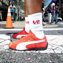 Load image into Gallery viewer, Person wearing red and white sneakers with a visible brand logo on a city street.