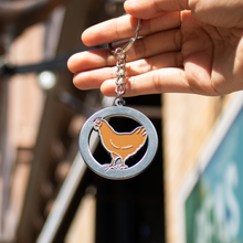 Load image into Gallery viewer, Hand holding a keychain with a chicken design against a blurred background
