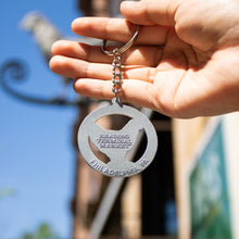 Load image into Gallery viewer, Hand holding a keychain with text against a blurred outdoor background

