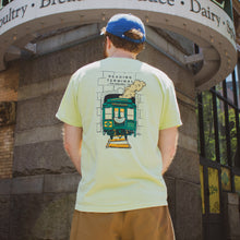 Load image into Gallery viewer, Person wearing a light yellow t-shirt with a train graphic, standing in front of a stone archway.

