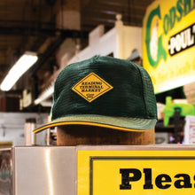 Load image into Gallery viewer, Green cap with a yellow patch on a counter in a market setting
