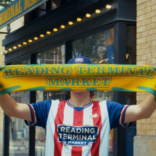 Load image into Gallery viewer, Person wearing a 'Reading Terminal Market' scarf and jersey in front of a building entrance.
